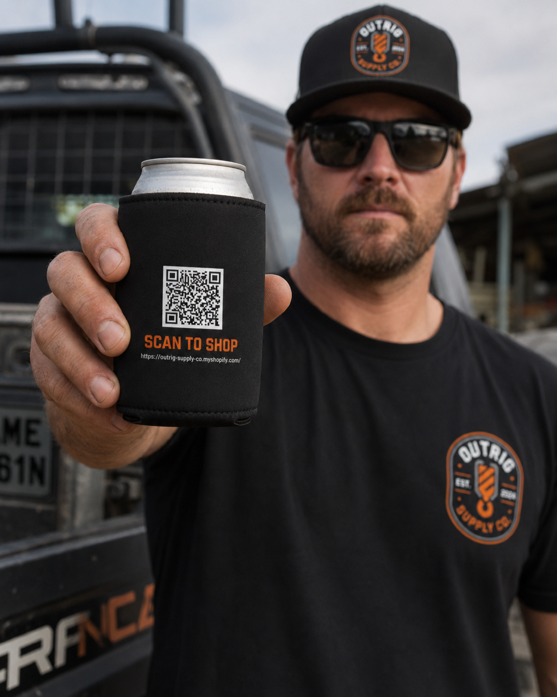 Man holding an Outrig Supply Co stubby cooler showing a QR code, wearing a black Outrig cap and T-shirt.