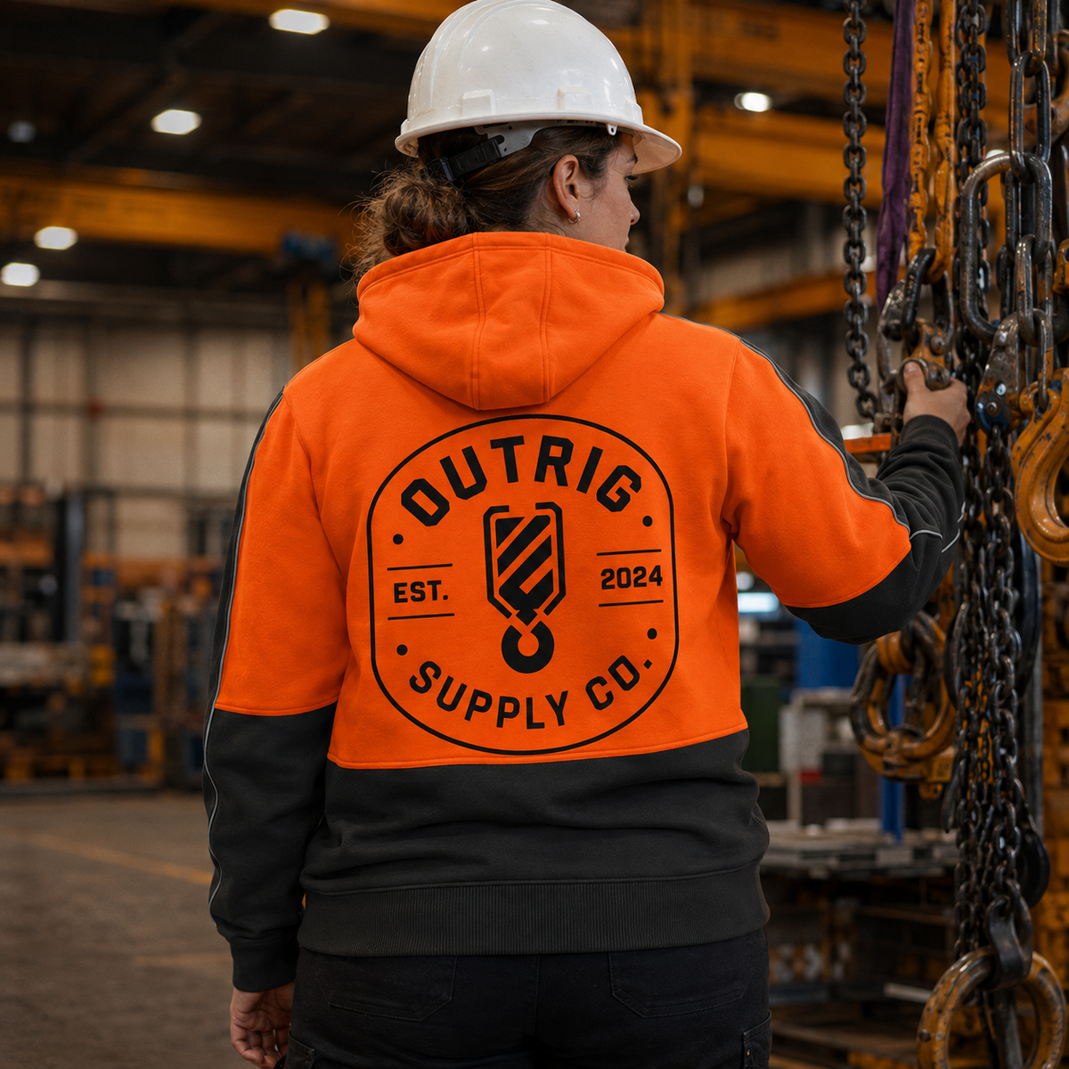 Rear view of the Outrig Supply Co orange and charcoal hi vis hoodie showing the large back logo in a workshop